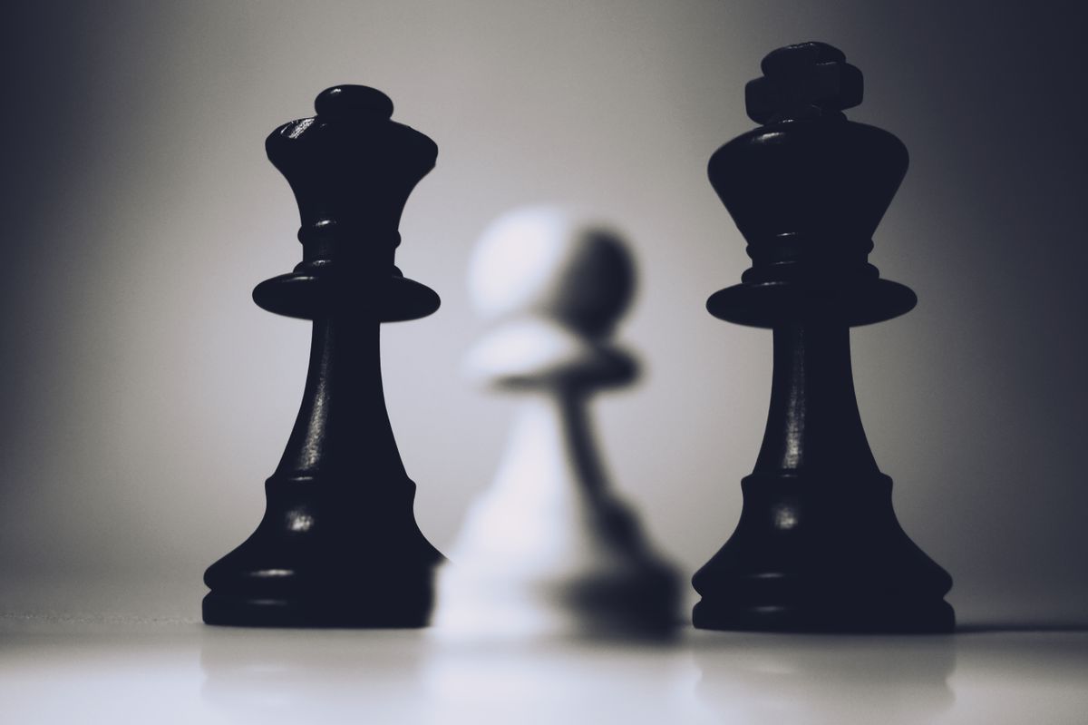Two black chess pieces — queen and king — foregrounded with a blurred white pawn behind. Visual metaphor for the enterprise AI integrator layer still owning the board.